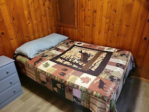 Una habitación con paneles de madera, una cama, un cojín azul y un aparador azul.