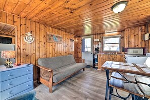 L’intérieur d’un chalet en bois, avec un canapé, une table à manger, un coin cuisine et une horloge au mur.