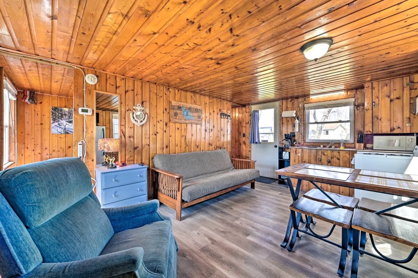 A cabin interior with a sofa, a dining table, a kitchen area, and wooden walls.