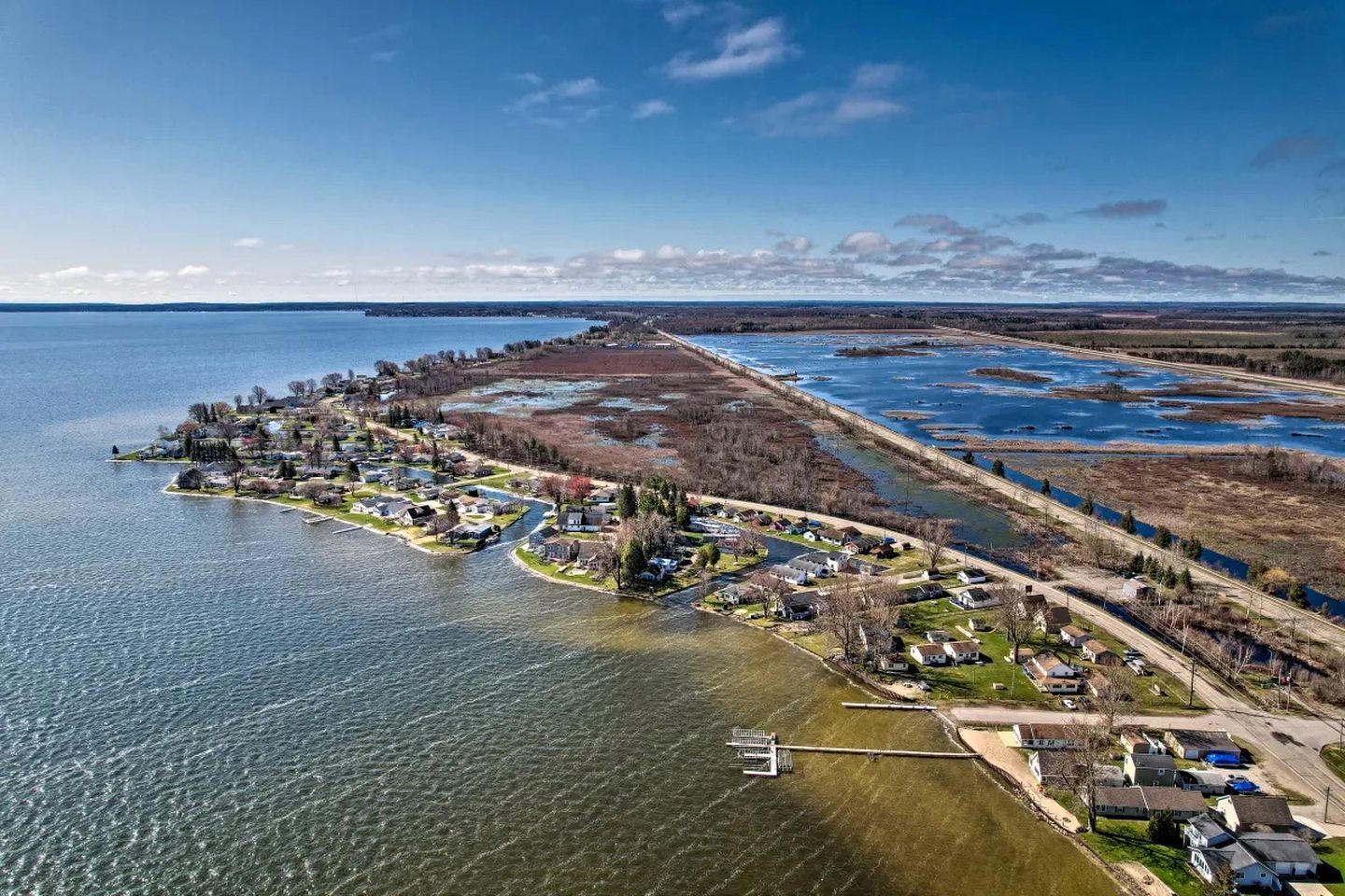 An aerial view of a lakeside community with residential areas, a dock, and a road leading to the water.