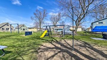 A playground with a yellow slide and swings, surrounded by houses and trees.