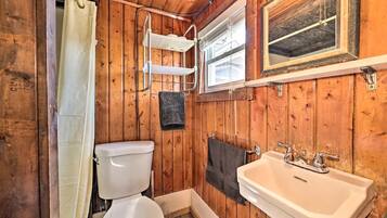 A wooden cabin bathroom with a toilet, shower, sink, and a window.