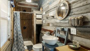 A rustic bathroom with a wooden wall, a white sink, a toilet, and a shower curtain.