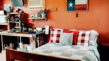 A bedroom with a bed, a desk with a computer, a shelf with kitchen items, and a Texas flag.