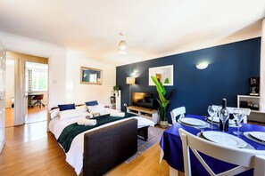 A modern hotel room with a bed, a dining table set for two, a TV, and a desk with a chair. - Stylish Apt·Canals·2 x Free Parking·Sleeps 6 (Birmingham)