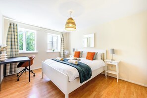 Ein Schlafzimmer mit Bett, Nachttisch, Lampe und Schreibtisch mit Stuhl.