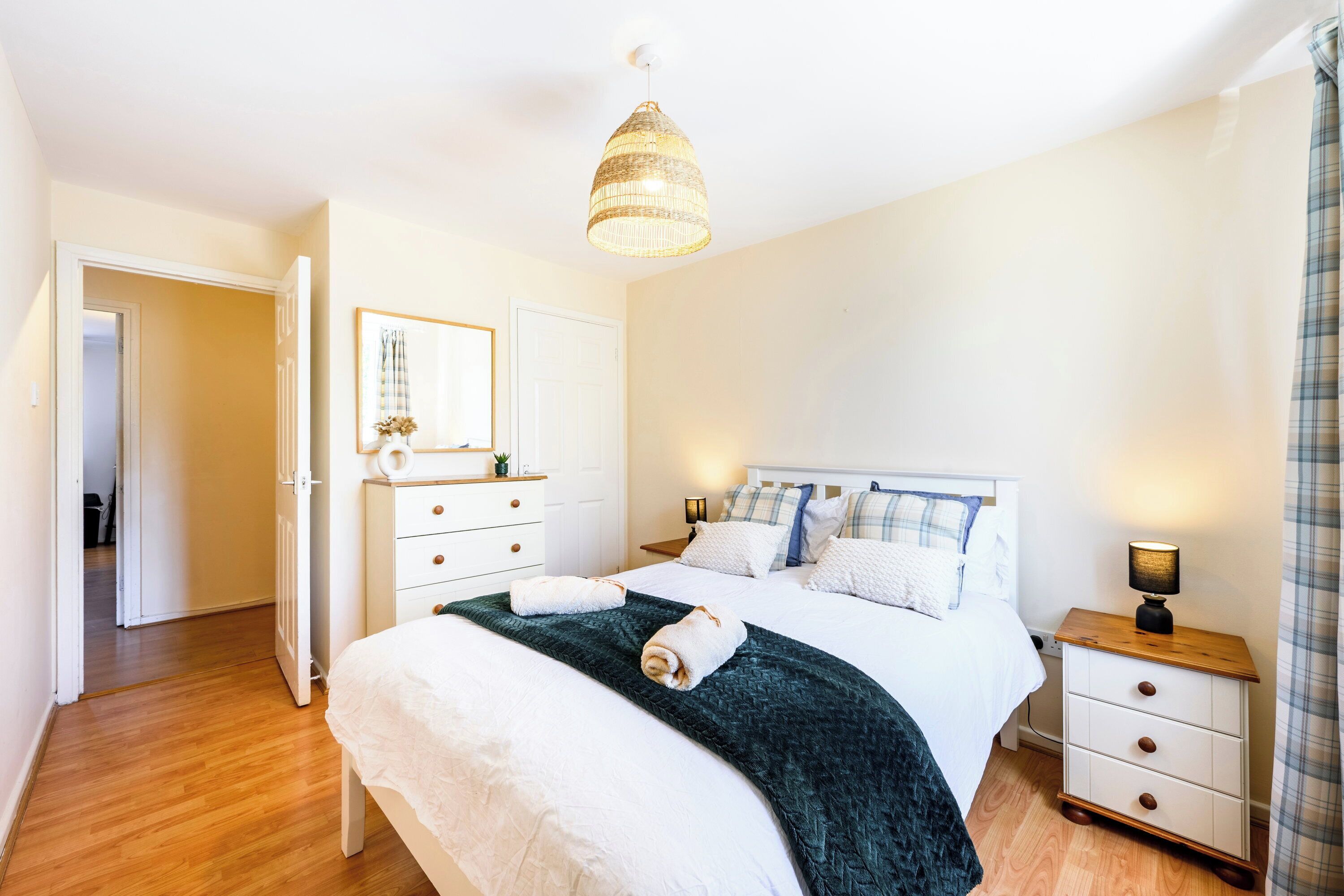Een slaapkamer met een bed, nachtkastje, lamp en een deur naar een andere kamer.