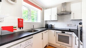 Ett modernt kök med vita skåp, en svart bänkskiva, en rostfri köksfläkt, en inbyggd ugn och en diskmaskin.