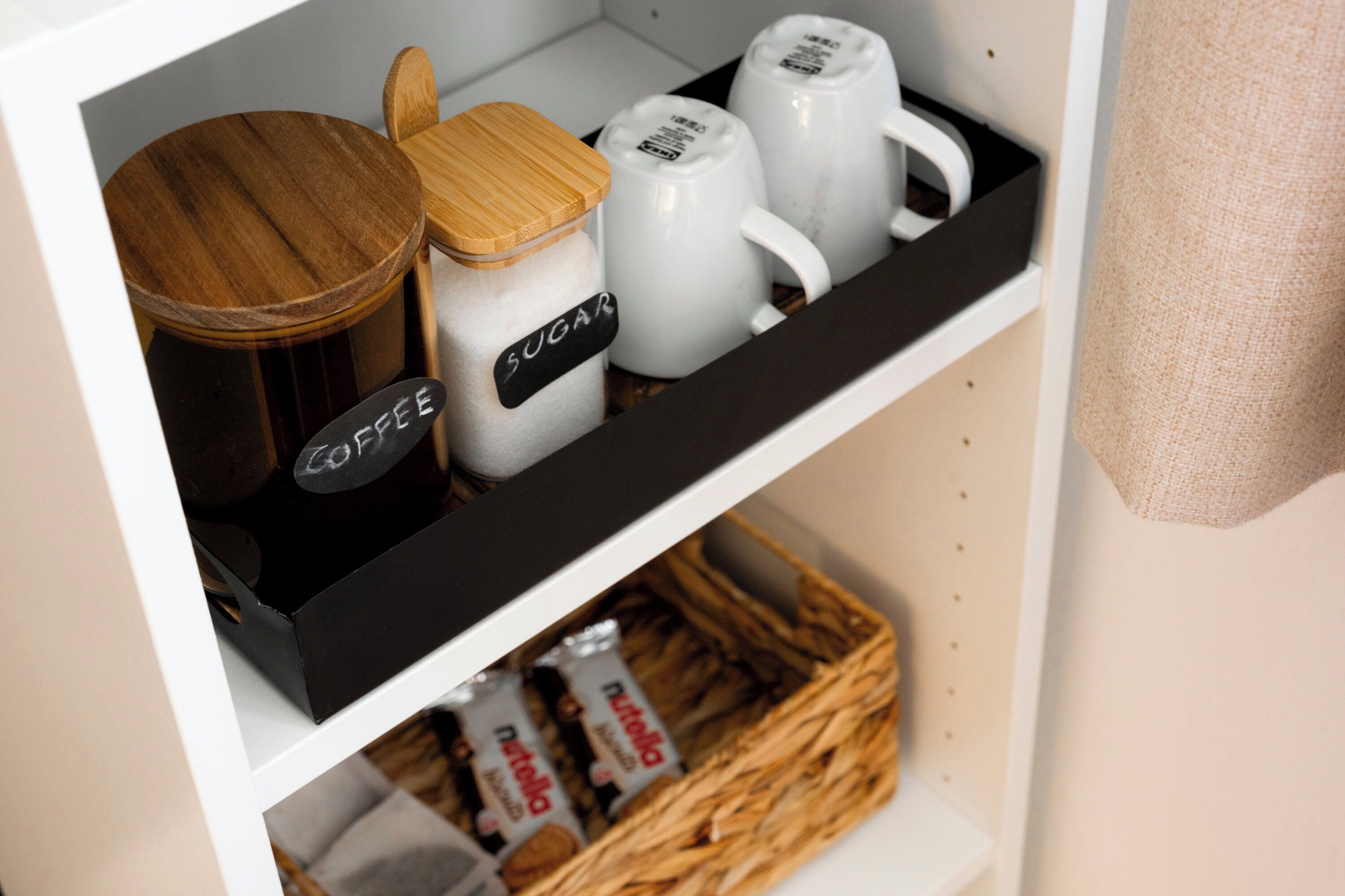 Een plank met gemarkeerde verpakkingen suiker en koffie, een houten pot en een mandje met Nutella.