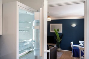 Eine moderne Küche mit einem weißen Bosch-Kühlschrank, einem Essbereich mit blauer Tischdecke und einer dunkelblauen Wand.