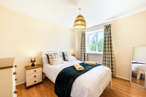 A bedroom with a bed, bedside table, lamp, window with curtains, and a hanging light fixture. - Stylish Apt·Canals·2 x Free Parking·Sleeps 6 (Birmingham)