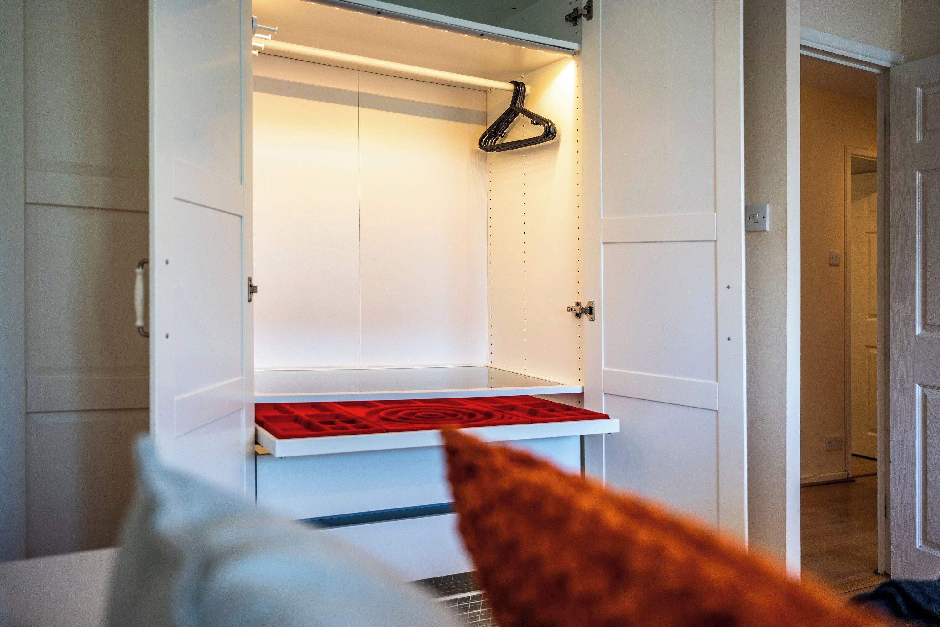 A white closet with a red mat at the bottom, a hanging rod, and a door with a handle.