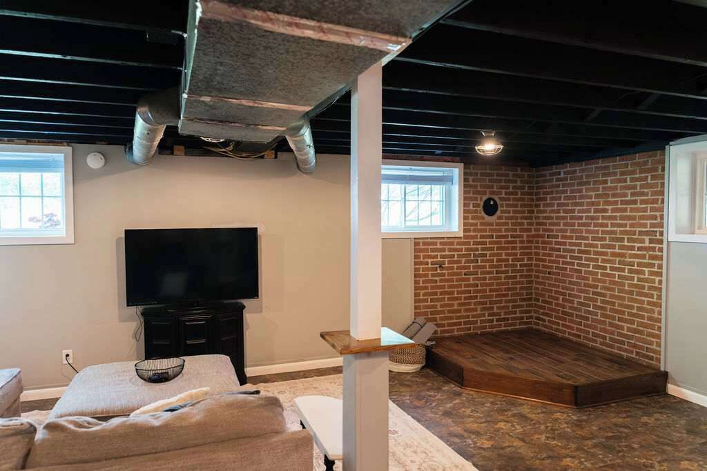 A room with a brick wall, a television, a wooden platform, and a window.