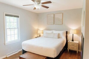 Ein Schlafzimmer mit einem Bett, zwei Nachttischen, einem Deckenventilator und zwei an der Wand befestigten Kunstwerken.