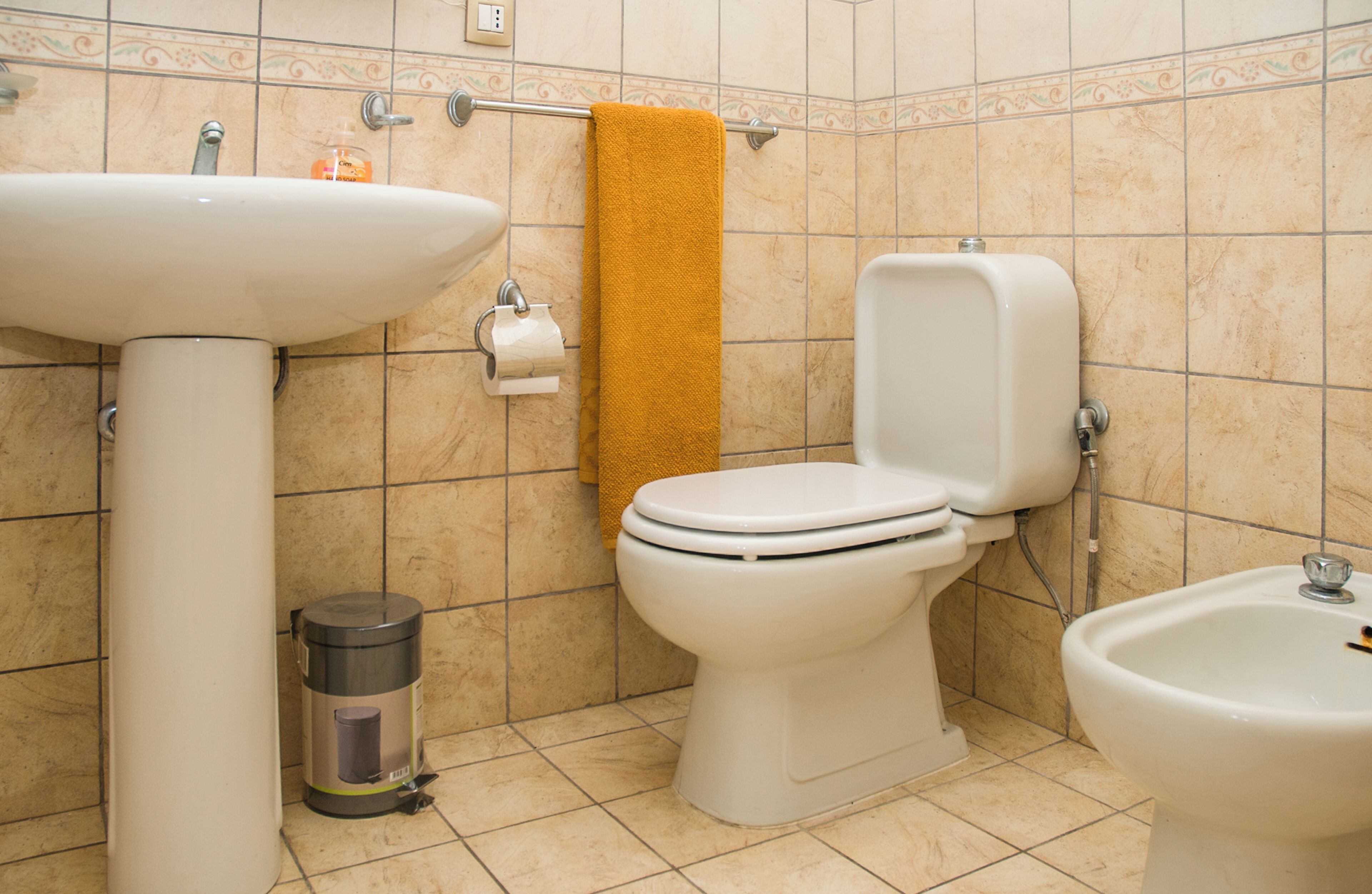 A bathroom with a sink, toilet, bidet, and trash can.