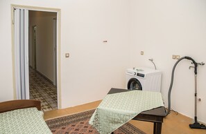 Ein Zimmer mit Bett, Tisch, Waschmaschine und Staubsauger.