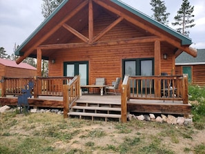 Una cabaña de troncos con una terraza de madera, un porche delantero y un comedor.