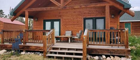 A log cabin with a wooden deck, a front porch, and a dining area.