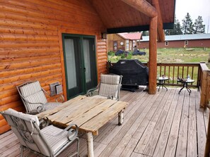 A wooden deck with a table and chairs, a grill, and a covered area with a view of a house in the background.