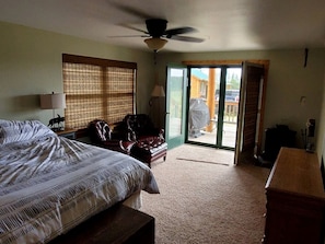 A bedroom with a bed, a chair, a desk, a ceiling fan, and a sliding glass door leading to an outdoor area.