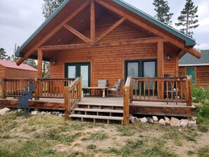 A log cabin with a wooden deck, a front porch, and a dining area. - Beautiful Cabin with Fire Pit and Deck in Foxpark, Wyoming (Foxpark)
