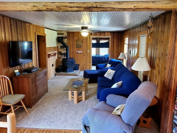 A cozy cabin interior with a sofa, television, wooden furniture, and a fireplace.