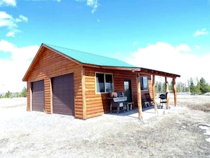 A log cabin with a covered porch, a grill, and a small table.