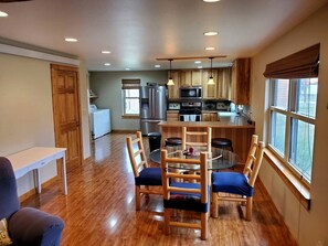 A modern kitchen with wooden cabinets, a stainless steel refrigerator, and a microwave. There is a dining area with a round table and chairs.