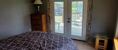 Un dormitorio con una cama, un aparador, una lámpara y un ventanal corredera que da a un espacio exterior.