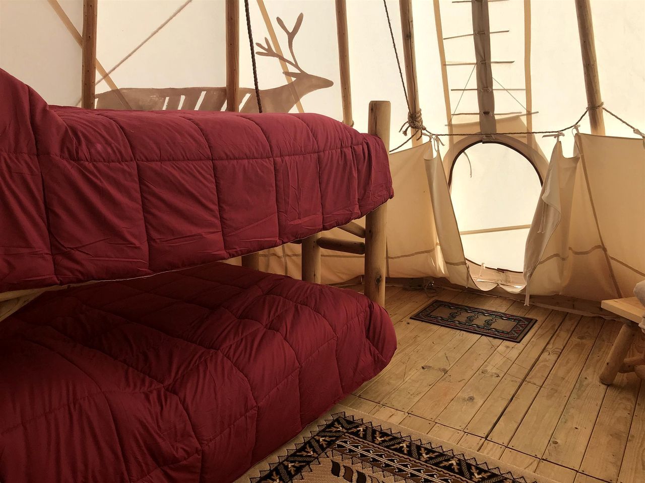 A tent with a wooden floor, a red bed, and a deer silhouette on the wall.