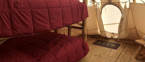 A tent with a wooden floor, a red bed, and a deer silhouette on the wall.