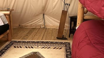 Ein Zeltraum mit einem roten Bett, einem gemusterten Teppich, einer Lampe und einem Holzbstuhl.