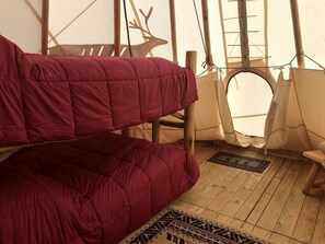 Una carpa con suelo de madera, una cama roja y la silueta de un ciervo en la pared.
