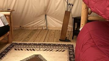 A tented room with a red bed, a patterned rug, a lamp, and a wooden chair.