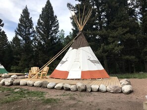 Un tipi cónico decorado con motivos animales, una terraza de madera y una silla.