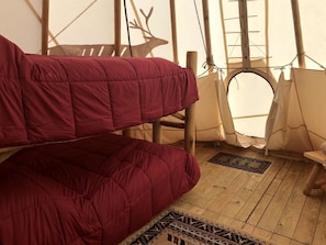 Ein Zelt mit Holzboden, einem roten Bett und einer Hirschsilhouette an der Wand.