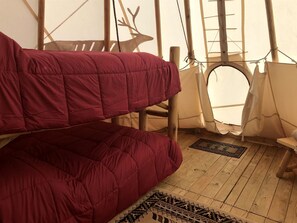 A tent with a wooden floor, a red bed, and a deer silhouette on the wall.