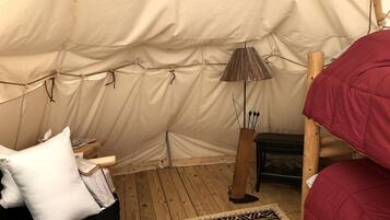 A tent interior with a bed, pillows, a lamp, a fire pit, and a rug.