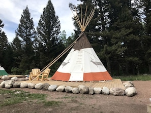 A conical teepee with animal designs, a wooden deck, and a chair.