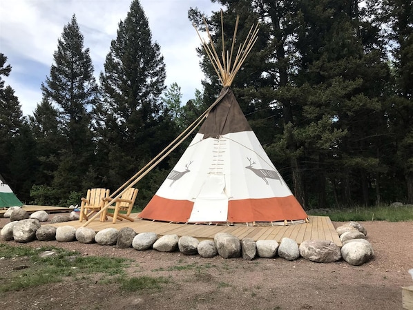 A conical teepee with animal designs, a wooden deck, and a chair.
