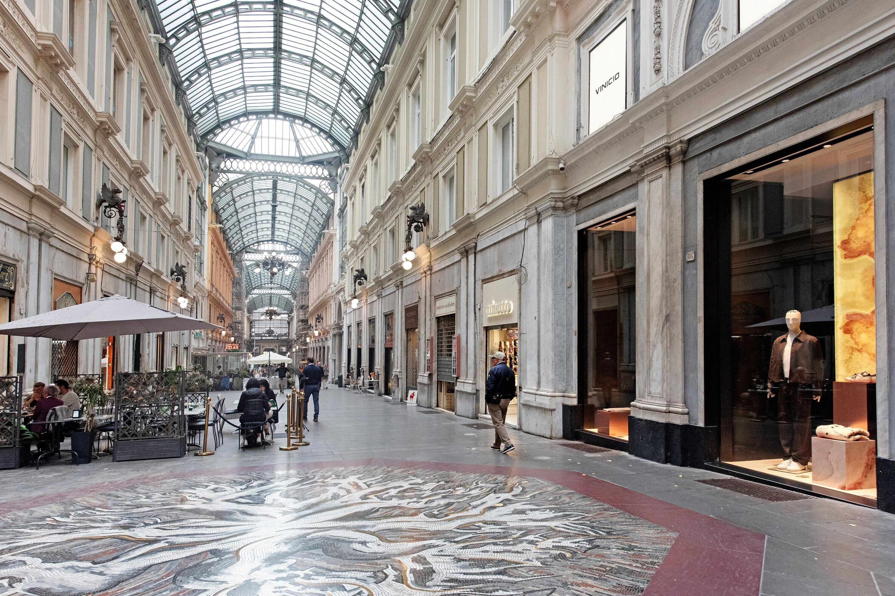 A spacious indoor area with a high ceiling and a glass roof, featuring a central walkway and shops on either side.