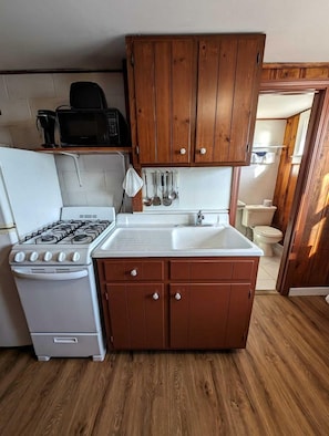 A compact kitchen with wooden cabinets, a white sink, a stove, and a microwave. - Refined Coastal Retreat with Panoramic Sea Views in North Truro, Massachusetts (North Truro)