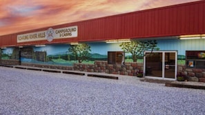 A campground with a red building, a mural of a landscape, and a gravel parking area.