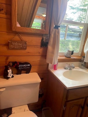 A wooden cabin bathroom with a toilet, sink, and window with curtains.