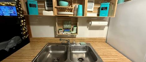A kitchen with two stainless steel sinks, wooden countertops, and teal storage containers.