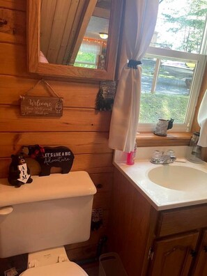 Un baño de cabaña de madera con inodoro, lavabo y ventana con cortinas.