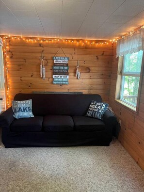 A cozy cabin interior with a wooden wall, string lights, a black sofa, and motivational wall decorations.