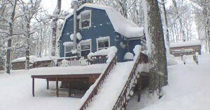 A snow-covered house with a wooden deck and stairs leading to a porch.