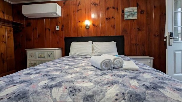 A bedroom with a bed, a nightstand, a dresser, and a wall-mounted air conditioner. - Bright Seaside Cottage with Panoramic Views in North Truro, Massachusetts (North Truro)