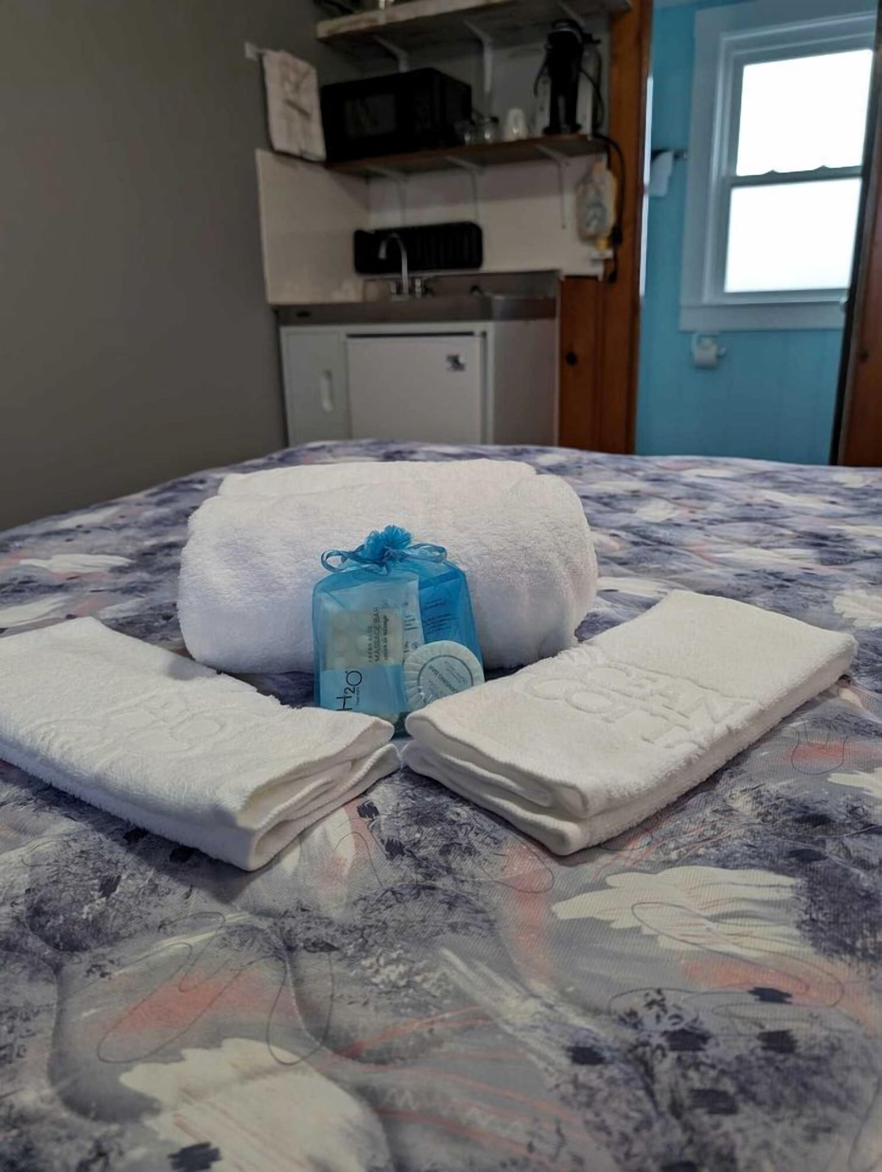 A bed with a floral bedspread, two neatly folded white towels, and a blue toiletry bag on it.